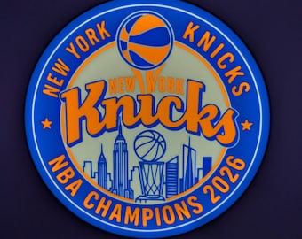 Pode incluir: Um letreiro de parede LED circular com o logótipo dos New York Knicks em azul e laranja. O design inclui uma bola de basquetebol, o nome da equipa, a silhueta do horizonte de Nova Iorque, um troféu e o texto New York Knicks NBA Champions 2026.