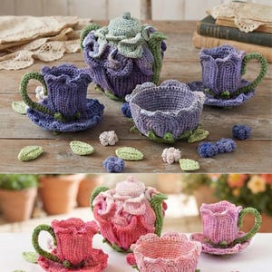 May include: Two sets of crocheted tea items featuring a teapot, two cups with saucers, and a bowl. One set is in shades of purple and green, while the other is in shades of pink and green. Each piece is shaped like a flower with textured petals.
