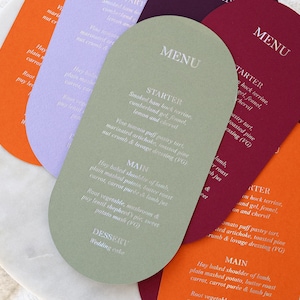 Può includere: Una collezione di biglietti di menu colorati e ad arco in tonalità arancione, viola, verde e bordeaux. Ogni biglietto presenta la parola "MENU" in alto e un elenco di voci di menu in testo bianco. I biglietti sono disposti su una superficie di marmo bianco.