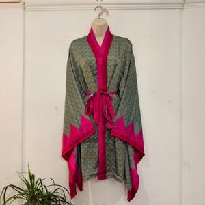 Könnte beinhalten: Ein grauer Kimono-Bademantel mit Muster, mit leuchtend pinkfarbenen Zierleisten und einem passenden Gürtel. Der Bademantel hat einen V-Ausschnitt und lange Ärmel. Die pinkfarbene Zierleiste hat ein Zickzack-Muster an den Kanten der Ärmel und am unteren Saum.