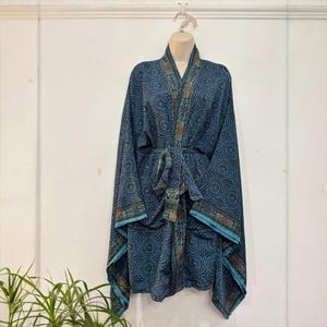 May include: A blue patterned robe with a matching belt, displayed on a hanger. The robe features a detailed circular design with accents of teal, orange, and brown. The robe's edges are trimmed with a teal border.