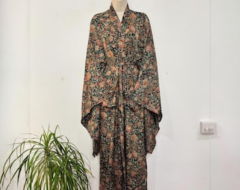 May include: A long, patterned kimono robe with a floral design in shades of green, brown, and red. The robe is hanging on a mannequin against a white wall. The robe has wide sleeves and a matching belt.
