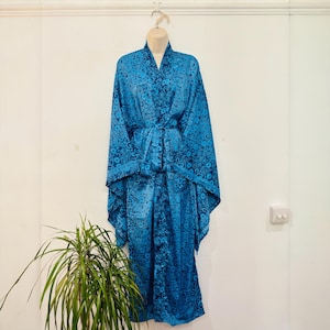 May include: A blue floral patterned robe with a matching belt, displayed on a mannequin. The robe has wide sleeves and a wrap-around design. The fabric has a shiny appearance. The robe is hanging against a white wall.