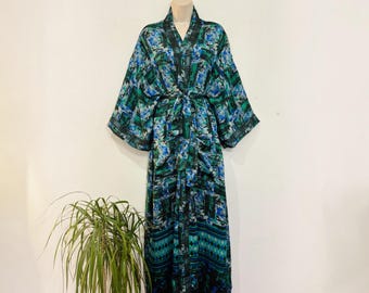 May include: A floor-length robe featuring a vibrant abstract pattern in shades of blue, green, and black. The garment has long, wide sleeves, a V-neckline, and a matching fabric tie belt at the waist. The hem displays a distinct geometric diamond pattern.