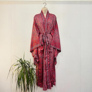 Könnte beinhalten: Ein langärmeliger Morgenmantel mit einem lebendigen, komplexen Paisley-Muster in Rot und Grau. Das Kleidungsstück verfügt über einen passenden Stoffgürtel in der Taille, weite Ärmel und einen Schalkragen, präsentiert an einer Schaufensterpuppe.