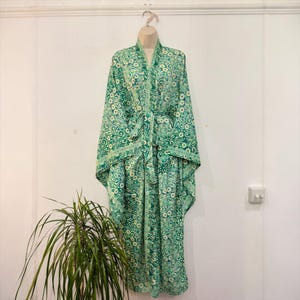 May include: A green floral patterned robe with a matching belt, hanging on a hanger. The robe features a white floral design on a green background. The robe is made of a lightweight fabric and has wide sleeves.