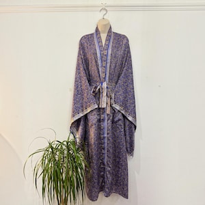 May include: A long-sleeved robe in a deep purple hue featuring an intricate gold floral pattern throughout. The garment includes a matching fabric tie belt at the waist and a contrasting vertical border design along the front opening and cuffs.