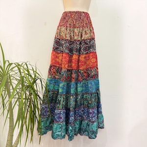 Op de afbeelding: Een enkellange rok met stroken en een levendig patchwork van paisley-patronen in tinten rood, oranje, blauw, groen en paars. Het kledingstuk heeft een geplooide, elastische tailleband en een vol, zwierig silhouet dat tot aan de enkels reikt.