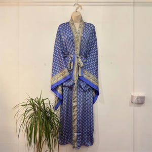 Op de afbeelding: Blauw patroon badjas met bijpassende strik, hangend aan een mannequin. De badjas heeft een herhalend paisley-ontwerp in blauw- en goudtinten. De badjas heeft wijde mouwen en een contrasterende blauwe bies.