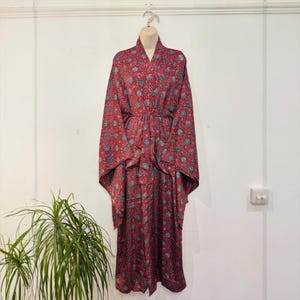 May include: A red kimono-style robe with a floral pattern in shades of blue and gray. The robe is hanging on a mannequin and has wide sleeves and a matching belt. The fabric appears to be lightweight.