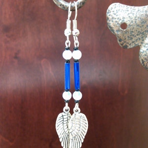 May include: Silver dangle earrings with blue and white beads and silver angel wings.