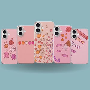 May include: Five pink phone cases with various designs. One case features ghosts, another strawberries, a third oranges and cherries, a fourth candy and chocolate, and the last shooting stars. The cases are arranged in a row.