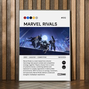 Pode incluir: Um poster emoldurado de "MARVEL RIVALS" com borda branca. A imagem mostra uma cena futurista com personagens. O texto inclui o título do jogo, a data 06/12/2024 e as palavras "HERO SHOOTER COMPETITIVE". O poster está em madeira.