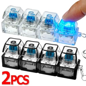 May include: Clear and black mechanical keyboard switches with blue internal components. One switch is illuminated with a bright blue light. The image includes the text "2PCS".