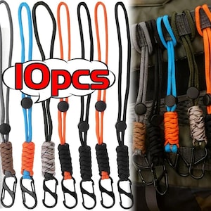Könnte beinhalten: Eine Sammlung von zehn Schlüsselbändern in verschiedenen Farben, darunter Schwarz, Orange, Blau und Grau. Jedes Schlüsselband hat einen schwarzen Karabiner und einen schwarzen Knopf. Der Text "10pcs" wird in einer weißen Sprechblase mit roter Umrandung angezeigt.