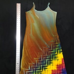 May include: A long, sleeveless dress with a tie-dye pattern in shades of blue, green, yellow, orange, red, and purple. The dress has a chevron pattern on the bottom half.