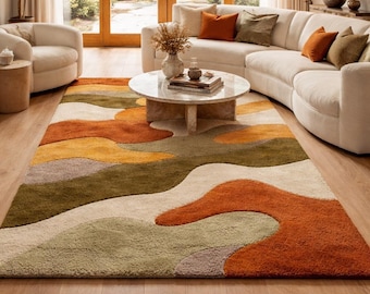 Könnte beinhalten: Ein großer, abstrakter Teppich mit einem wellenförmigen Design in Orange-, Grün-, Gelb- und Beigetönen. Der Teppich befindet sich in einem Wohnzimmer mit einem weißen Sofa, einem runden Couchtisch und Holzböden. Der Raum hat große Fenster und natürliches Licht. Ungefähr 240 cm x 300 cm.