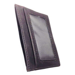 May include: A dark brown leather cardholder with a clear plastic window. The cardholder has a slim design with visible stitching around the edges. The interior is lined with a textured fabric.