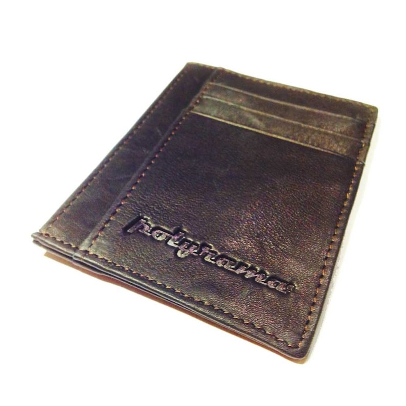 May include: A dark brown leather wallet with visible card slots. The wallet has a stitched border and the word "polypharma" is embossed on the front. The wallet is rectangular and appears to be new.