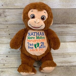 May include: A brown plush monkey with embroidered details. The monkey has a smiling face and is holding a sign with the name "Nathan Marc Mu&ntilde;oz", birthdate, weight, length (21 inches), and time of birth.