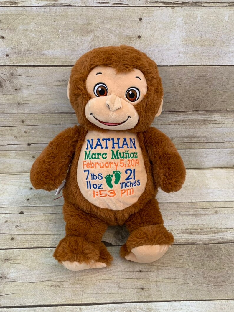 May include: A brown plush monkey with embroidered details. The monkey has a smiling face and is holding a sign with the name "Nathan Marc Mu&ntilde;oz", birthdate, weight, length (21 inches), and time of birth.