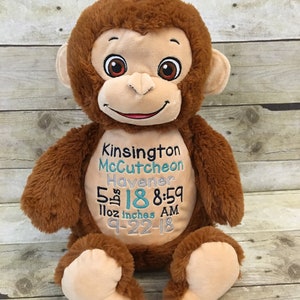 May include: A plush brown monkey with embroidered details. The monkey has a tan face, ears, and feet. Text on the monkey's belly includes a name, date, time, weight, and height: 5 lbs 18 inches 8:59 AM.