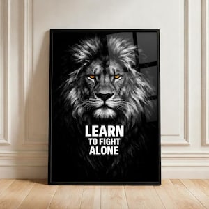 May include: Black framed wall art featuring a detailed grayscale lion portrait with piercing yellow eyes. The text "LEARN TO FIGHT ALONE" is displayed in white block letters. The artwork is set against a black background.