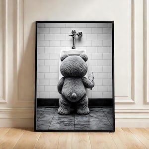 May include: A framed black and white wall art print featuring a textured gray teddy bear standing in front of a white porcelain urinal mounted on a tiled wall. The bear is holding a clear plastic water bottle in its right hand, facing the wall.