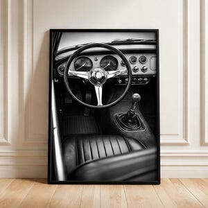 Pode incluir: Impressão em preto e branco do interior de um carro clássico. A imagem apresenta um volante, um painel com mostradores, uma alavanca de câmbio e um assento de couro. O interior é detalhado com detalhes cromados.