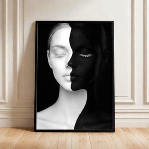 Może przedstawiać: Oprawiony wydruk artystyczny przedstawiający twarz kobiety podzieloną pionowo, z jedną połową białą, a drugą czarną. Oczy kobiety są zamknięte, z białymi rzęsami po czarnej stronie. Kontrastowe czarno-białe dzieło sztuki.