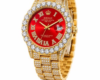 May include: A gold-tone automatic watch with a vibrant red dial, featuring Roman numeral hour markers, a date window at the three o'clock position, and a crown logo. The bezel and link bracelet are encrusted with clear stones.