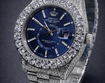May include: A luxury wristwatch with a blue face and a diamond-encrusted bezel and band. The watch face displays the brand "JORDAN", the text "SAPPHIRE CRYSTAL TIME JUST", and the date. The watch is an automatic high-quality watch.