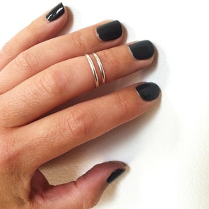 May include: A silver double band ring worn on a finger with black nail polish.