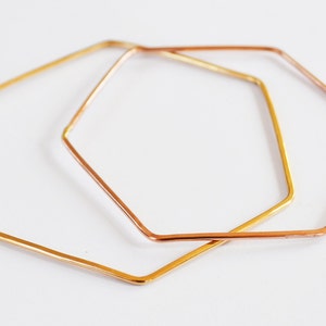 May include: Two hexagon-shaped bracelets, one gold and one rose gold, are stacked on top of each other.