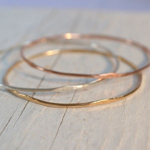 May include: Three gold bangles stacked on top of each other. The bangles are made of different metals: gold, silver, and rose gold. The bangles are all hammered and have a textured finish.