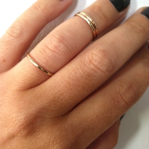 May include: A hand wearing three thin gold rings on the middle finger. The nails are painted black.