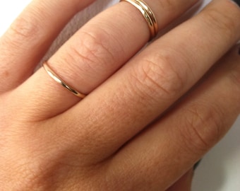 May include: A hand wearing three thin gold rings on the middle finger. The nails are painted black.