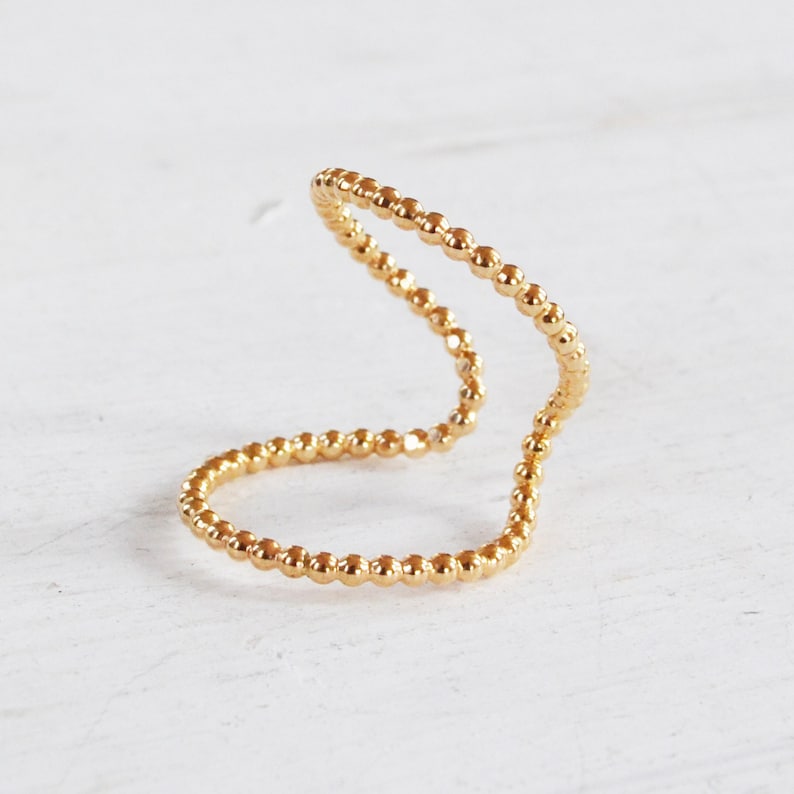 May include: A gold beaded ring with a unique open design. The ring is made of small, round beads that are connected together to form a continuous loop.