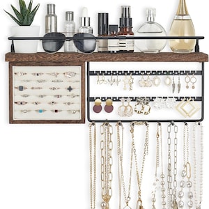 May include: A wooden and metal jewelry organizer with a shelf, ring display, earring rack, and necklace holders. The shelf holds sunglasses, perfumes, and a small potted plant. The organizer displays various rings, earrings, and necklaces in gold and silver tones.