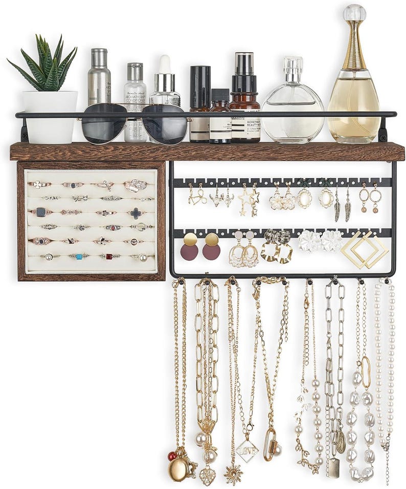 May include: A wooden and metal jewelry organizer with a shelf, ring display, earring rack, and necklace holders. The shelf holds sunglasses, perfumes, and a small potted plant. The organizer displays various rings, earrings, and necklaces in gold and silver tones.