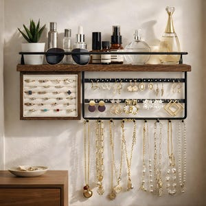 May include: A wooden and black metal jewelry organizer with a shelf holding sunglasses, skincare products, and a small potted plant. The organizer displays rings, earrings, and necklaces. The jewelry is gold and silver.