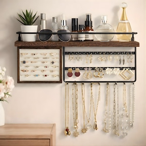 May include: A wall-mounted jewelry organizer with a dark wood shelf and black metal frame. The shelf holds sunglasses, perfumes, and a small potted plant. The organizer displays rings, earrings, and necklaces.