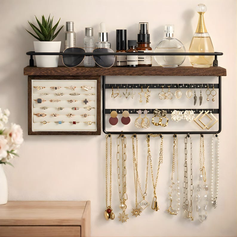 May include: A wall-mounted jewelry organizer with a dark wood shelf and black metal frame. The shelf holds sunglasses, perfumes, and a small potted plant. The organizer displays rings, earrings, and necklaces.