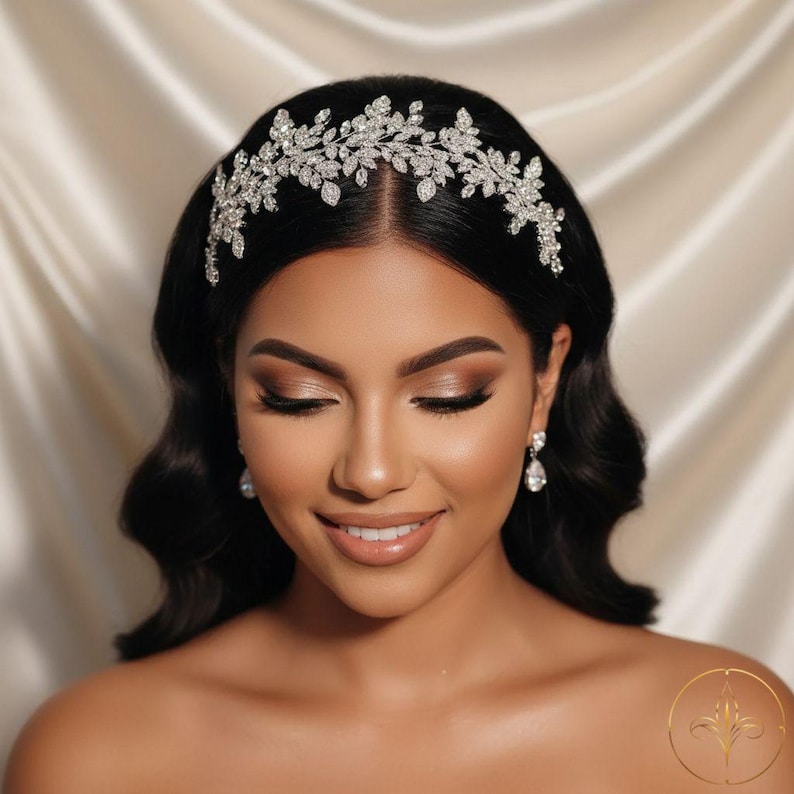 Puede incluir: Una mujer con cabello oscuro lleva una diadema plateada con un dise&ntilde;o floral. La diadema est&aacute; adornada con cristales brillantes. Tambi&eacute;n lleva aretes de cristal a juego. La mujer sonr&iacute;e con los ojos cerrados.