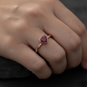 Puede incluir: Un anillo con una piedra preciosa de color rosa intenso en forma de coraz&oacute;n, montada en una banda de oro rosa pulido. La piedra est&aacute; asegurada en un engaste de bisel, creando un perfil suave y continuo en el dedo. La banda es fina y redondeada.
