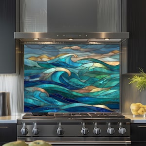 Könnte beinhalten: Eine Küchenrückwand aus Buntglas mit einem dynamischen Ozeanwellen-Design. Das Kunstwerk zeigt Farbtöne von Blau, Türkis und Gold und bildet einen künstlerischen Blickfang über einem Edelstahlherd. Die Rückwand ist zwischen schwarzen Schränken installiert.