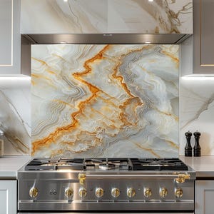 May include: A stainless steel gas range with gold-colored knobs and a decorative backsplash. The backsplash features a marble design with white, gray, and gold tones. Two black pepper grinders are on the countertop.