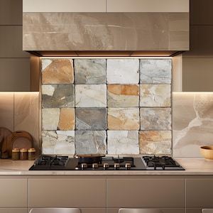 Op de afbeelding: Een moderne keuken met een zwart gaskookplaat en een pan, tegen een achterwand van veelkleurige stenen tegels. De kasten zijn neutraal beige, wat een moderne en stijlvolle uitstraling creëert.