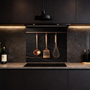Puede incluir: Una cocina moderna con gabinetes negros, una placa para salpicaduras de mármol y utensilios de cocina de color cobre colgando de una barra. Los utensilios incluyen un cucharón, una espátula y un batidor. Una placa de cocina negra y una lámpara colgante completan el diseño.