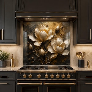 May include: A kitchen backsplash featuring a textured, three-dimensional relief of two large, blooming white and gold magnolia flowers with buds, set against a dark, mottled background, positioned behind a black and gold gas range stove.